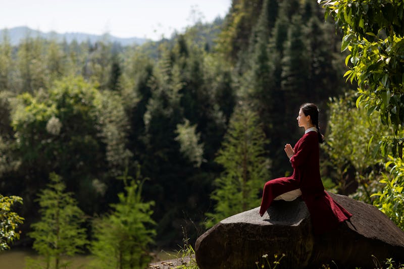 Mujer orando con ropa tradicional roja sentada en una roca marrón.